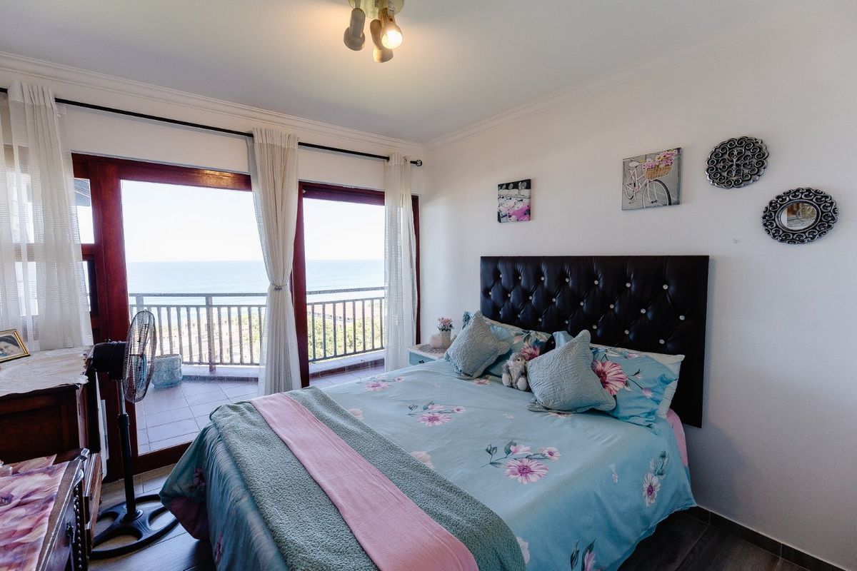 A bright bedroom featuring tiled flooring, cove molding, and large sliding glass doors that open onto a balcony with ocean views.