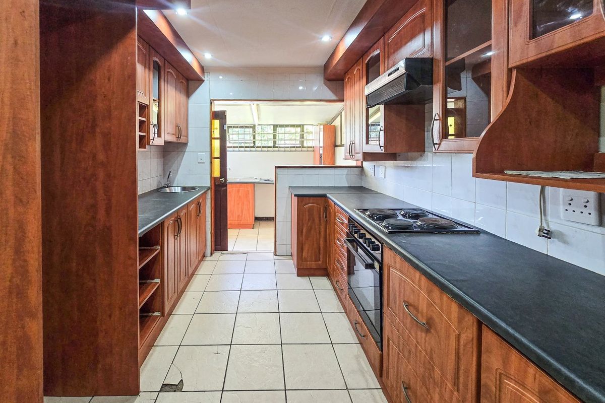 A galley-style kitchen featuring wooden cabinetry, dark laminate countertops, built-in oven, and hob, with a tiled floor and backsplash.