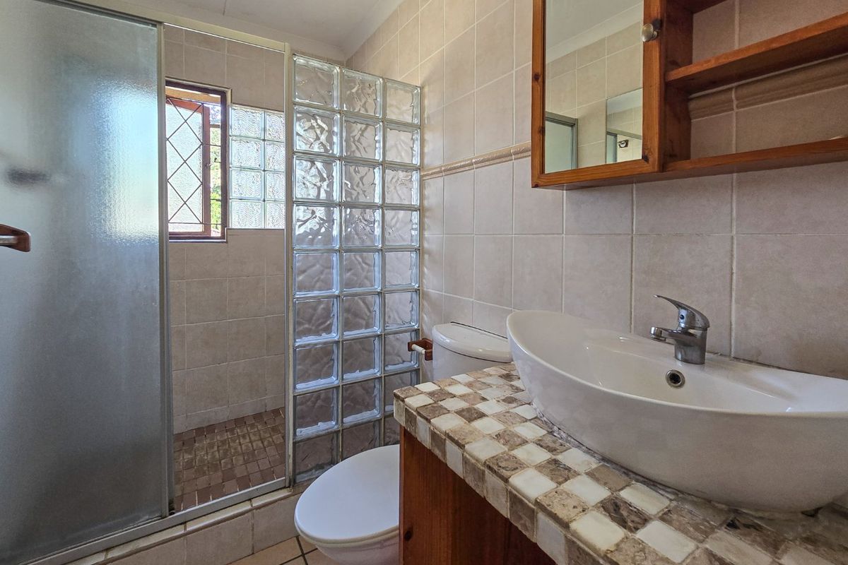 A functional bathroom featuring a glass block shower enclosure, vessel sink on a tiled vanity, and neutral wall tiling.