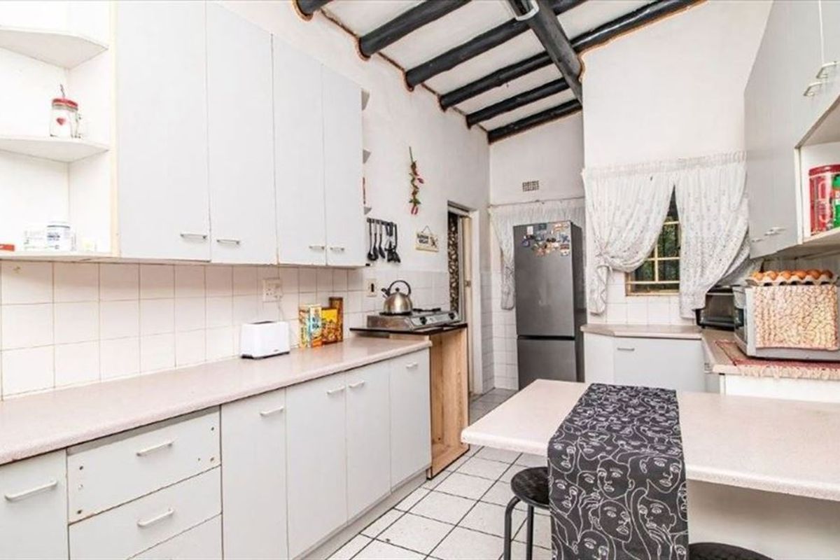 A functional kitchen featuring white built-in cabinetry, tiled flooring, a tiled backsplash, and rustic exposed ceiling beams.