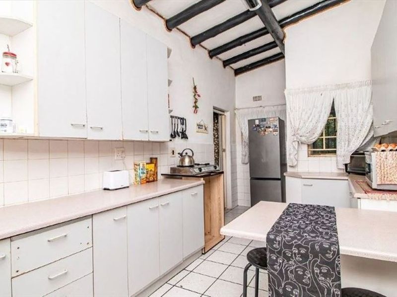 A functional kitchen featuring white built-in cabinetry, tiled flooring, a tiled backsplash, and rustic exposed ceiling beams.