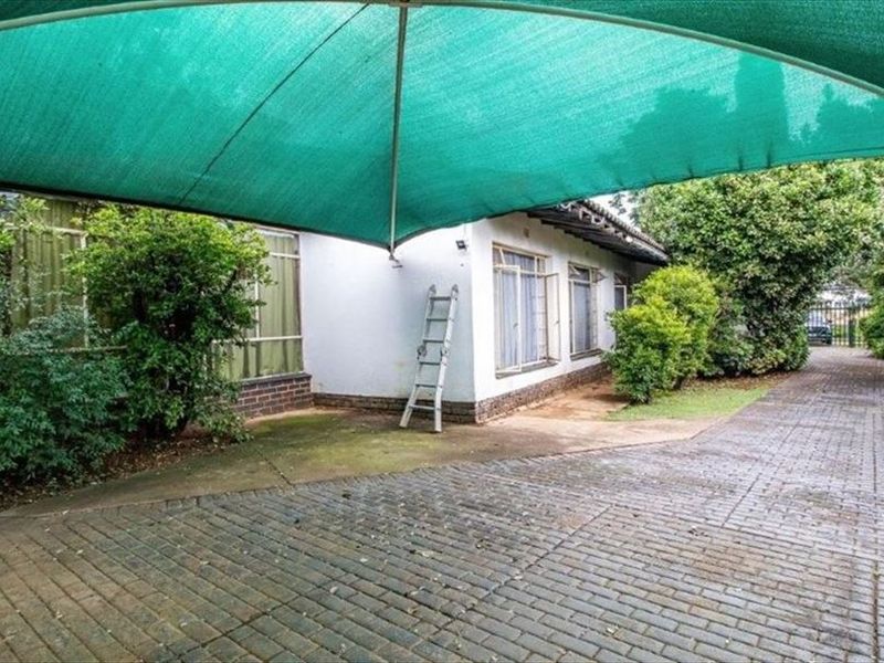 Front exterior view featuring a paved driveway and a large green shade sail covering the parking area.