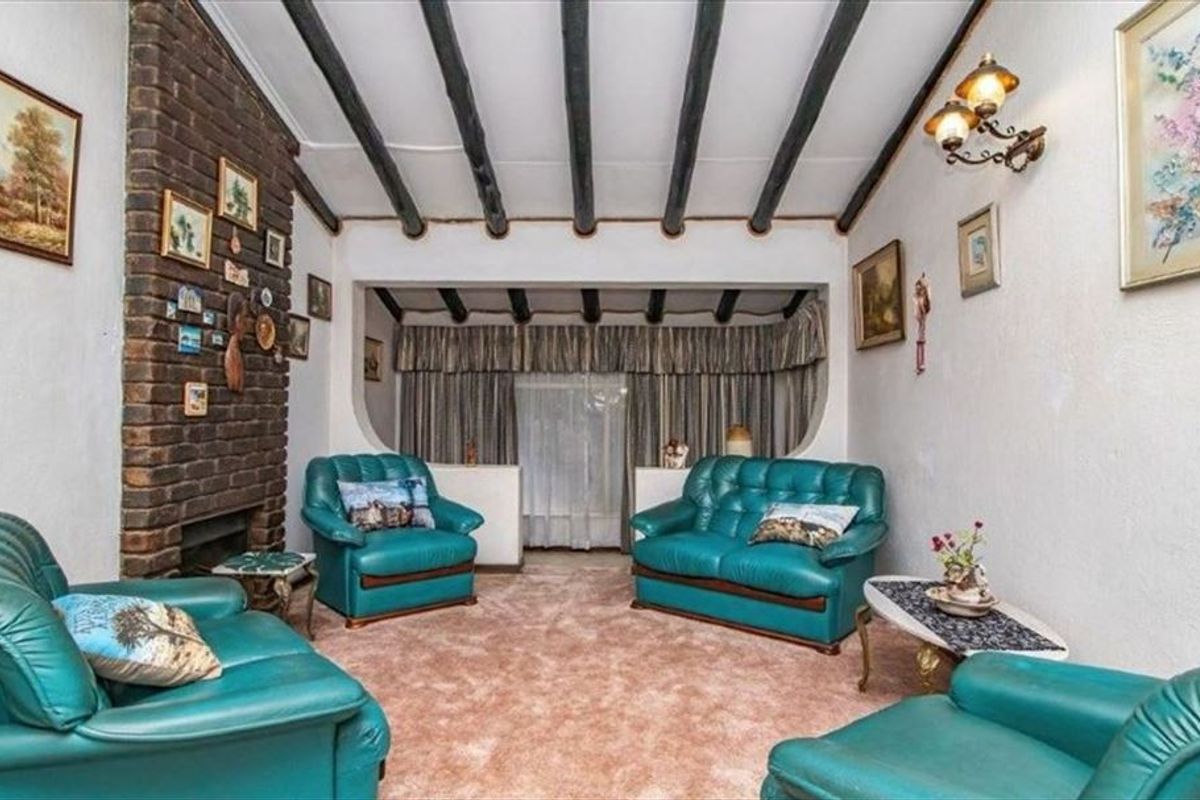 A traditional living room featuring a prominent brick fireplace and exposed timber ceiling beams, offering a cozy, dated aesthetic ready for modernization.
