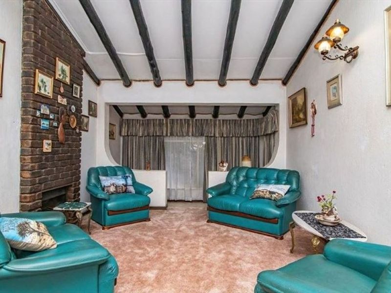 A traditional living room featuring a prominent brick fireplace and exposed timber ceiling beams, offering a cozy, dated aesthetic ready for modernization.