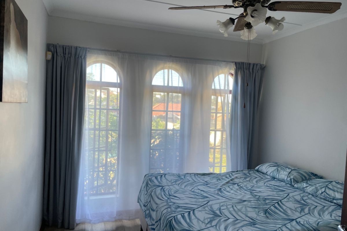 A bedroom featuring distinctive arched windows, a ceiling fan, and light-toned laminate flooring, offering a bright and functional living space.
