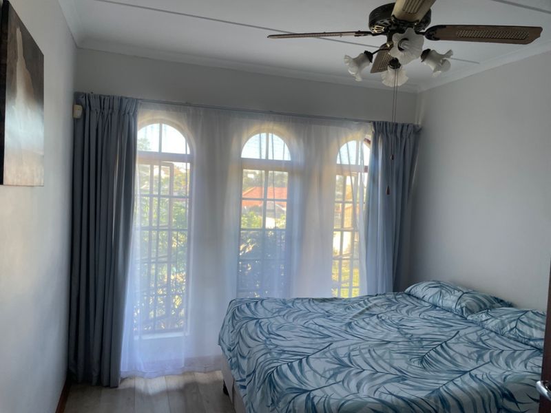 A bedroom featuring distinctive arched windows, a ceiling fan, and light-toned laminate flooring, offering a bright and functional living space.