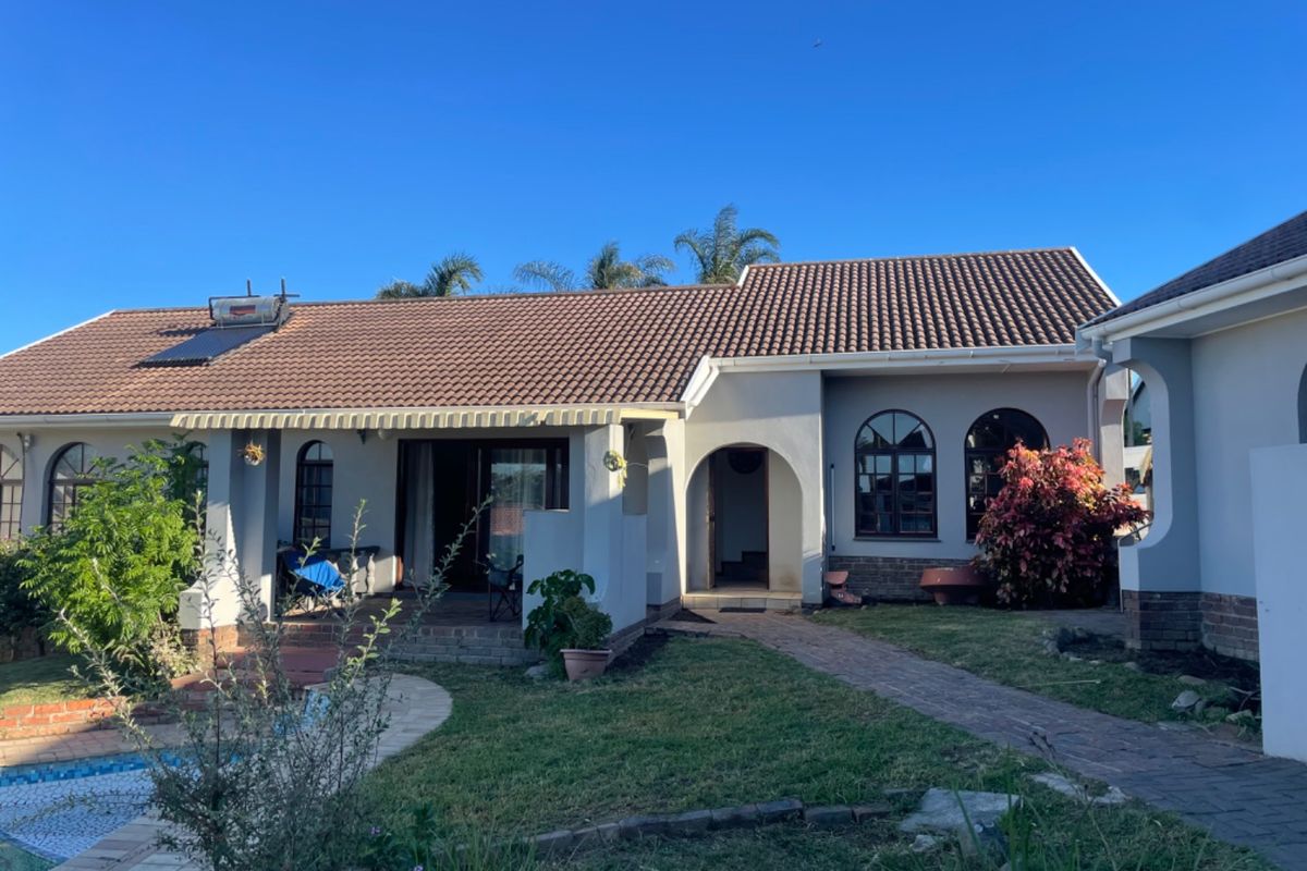 Rear view of the house featuring a tiled roof with solar water heater, arched windows, a covered patio, and a swimming pool.