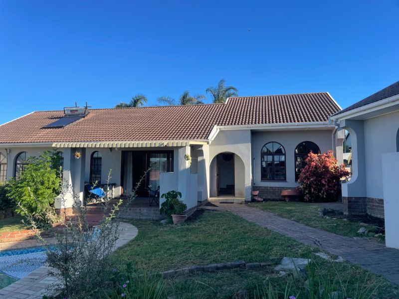 Rear view of the house featuring a tiled roof with solar water heater, arched windows, a covered patio, and a swimming pool.