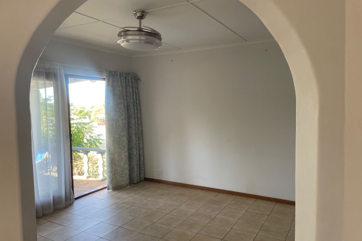 An empty living room featuring tiled flooring, a ceiling fan, and a sliding glass door providing access to an outdoor area.