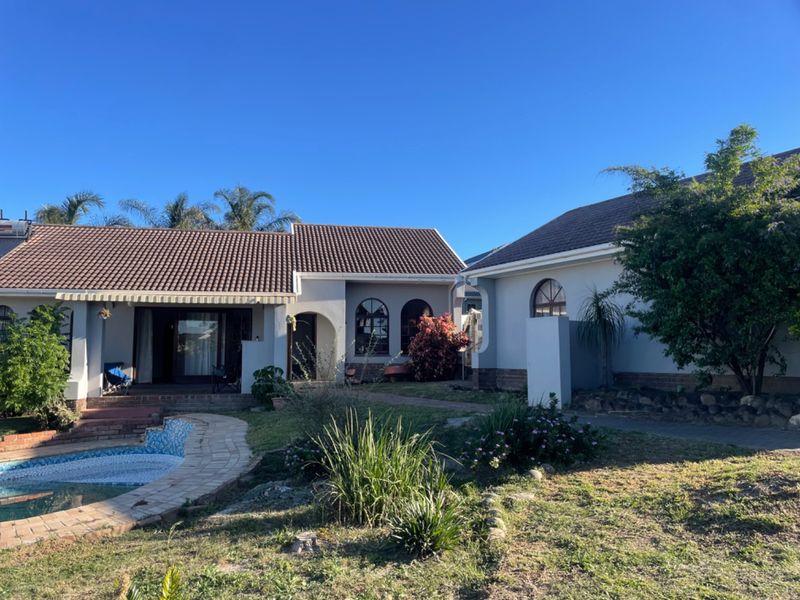 Rear view of the property featuring a tiled roof, covered patio area, and a swimming pool set within a landscaped garden.