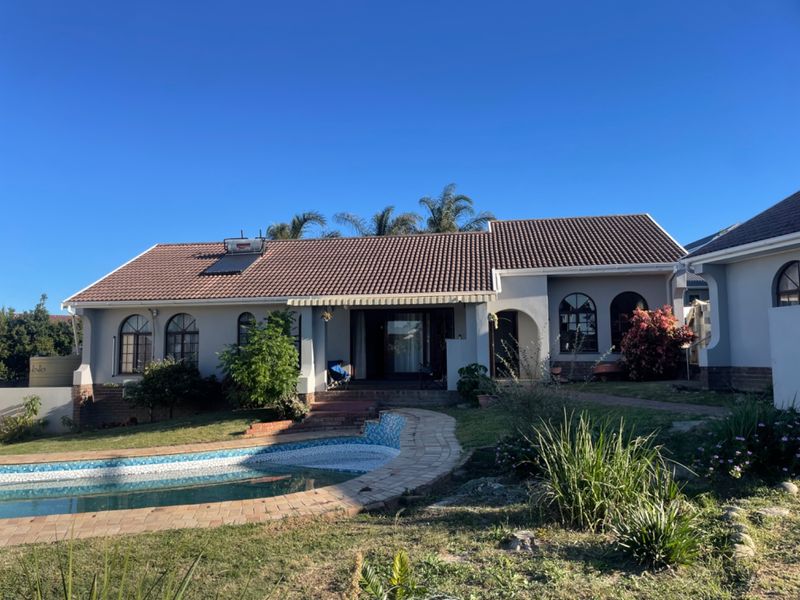 Rear view of the house featuring a tiled roof with solar water heater, arched windows, a covered patio, and a swimming pool with paved surround.