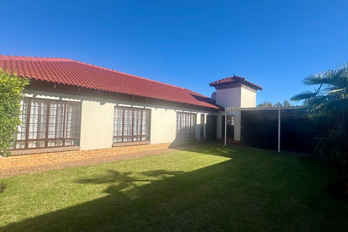 A well-maintained rear exterior view of the townhouse featuring a terracotta tiled roof, brick base detailing, a paved walkway, and a private lawn area.