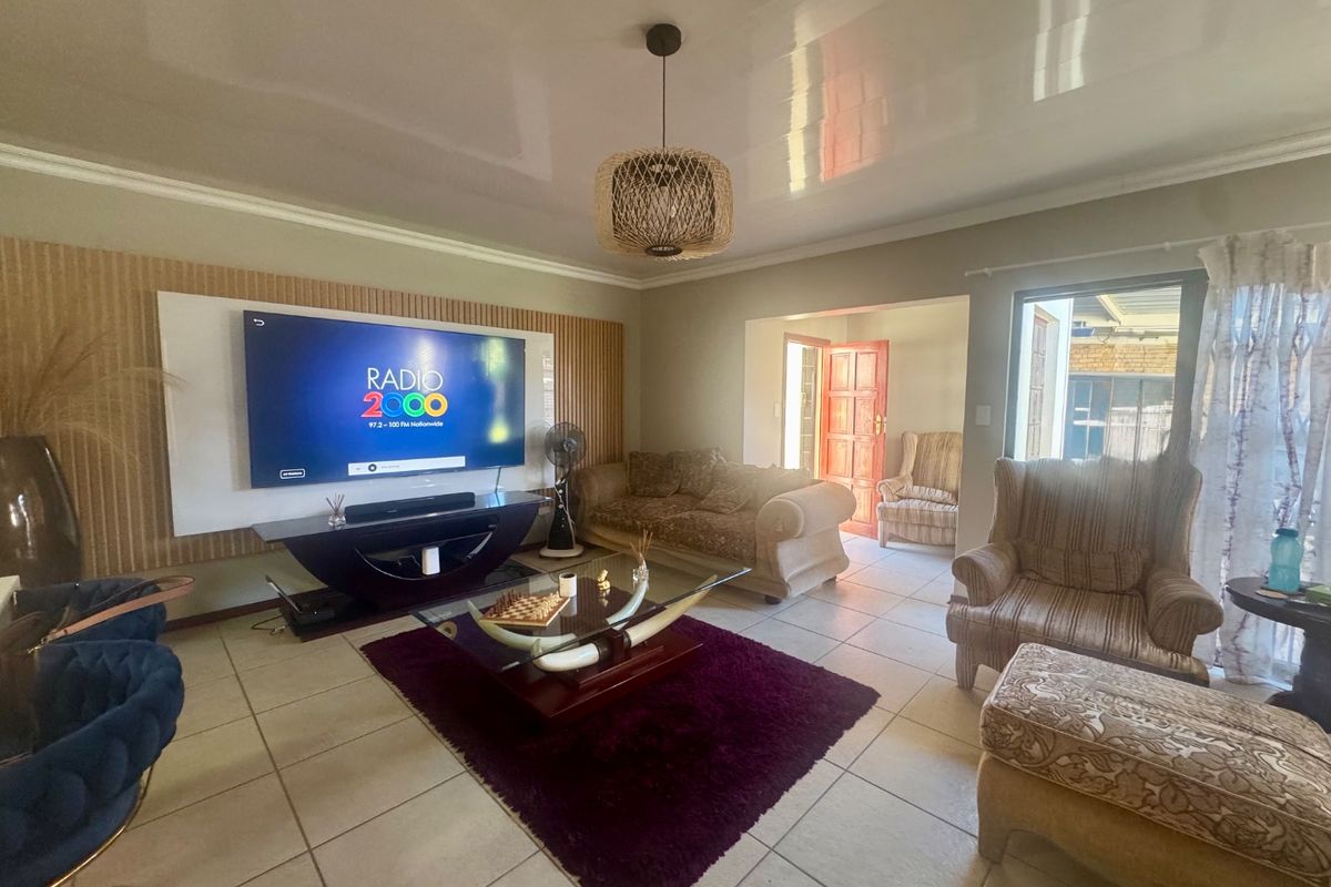 Spacious living room featuring tiled flooring, a glossy ceiling with cove molding, and a modern feature wall paneling design.