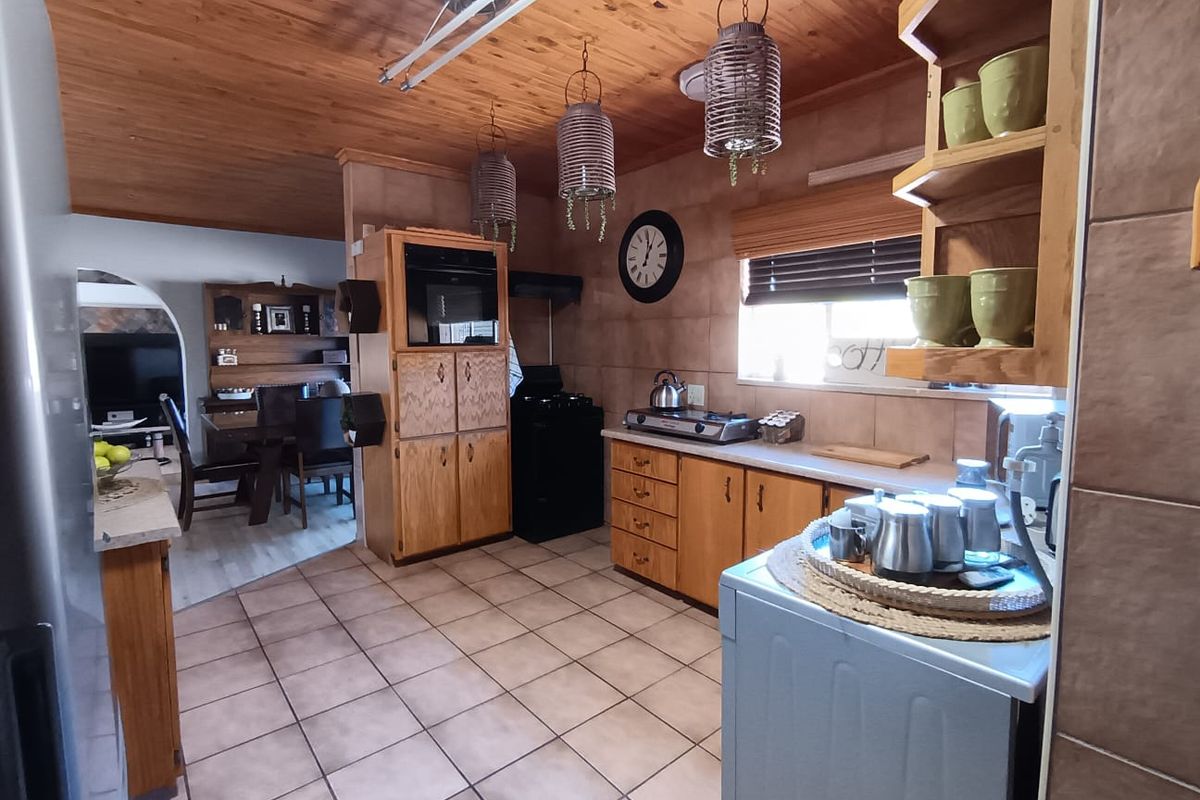 A functional kitchen featuring wooden cabinetry, tiled flooring, and a timber-clad ceiling, with an open-plan layout connecting to the adjacent dining area.