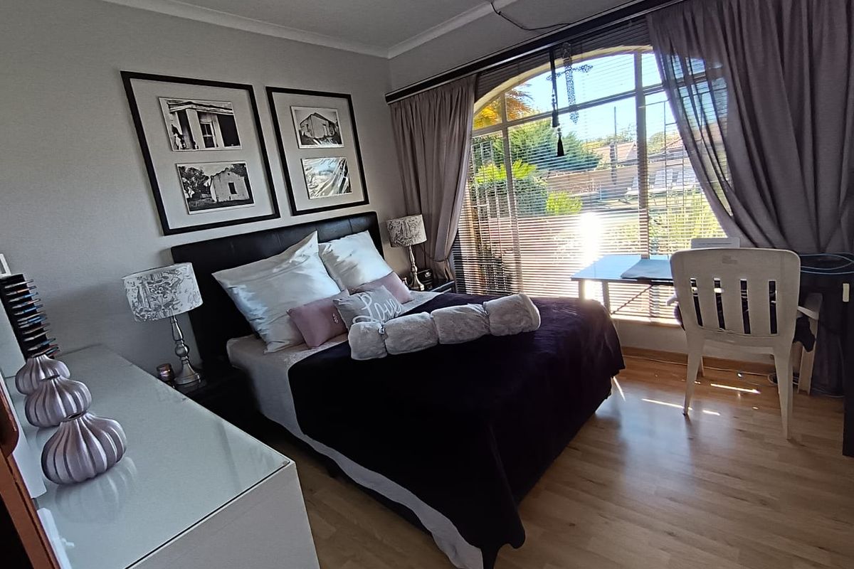 A bedroom featuring laminate flooring and a large arched window with integrated curtain tracks and visible surface-mounted electrical conduit.