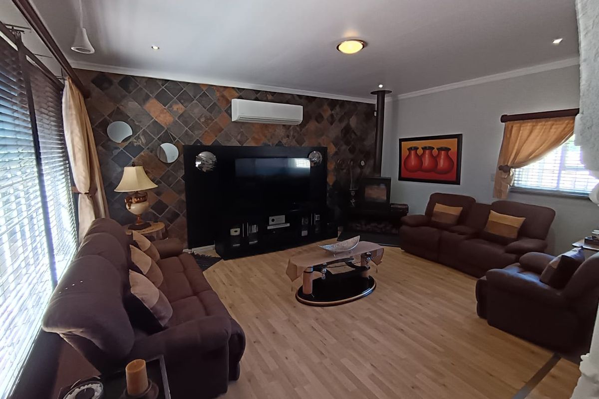 Spacious living room featuring a tiled feature wall, wood-burning fireplace, and split-system air conditioning, finished with light-toned laminate flooring.