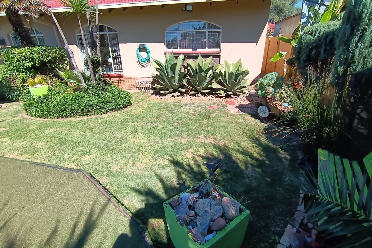 A well-maintained rear garden featuring a lush lawn, established succulent plantings, and a view of the home's rear facade with arched windows.