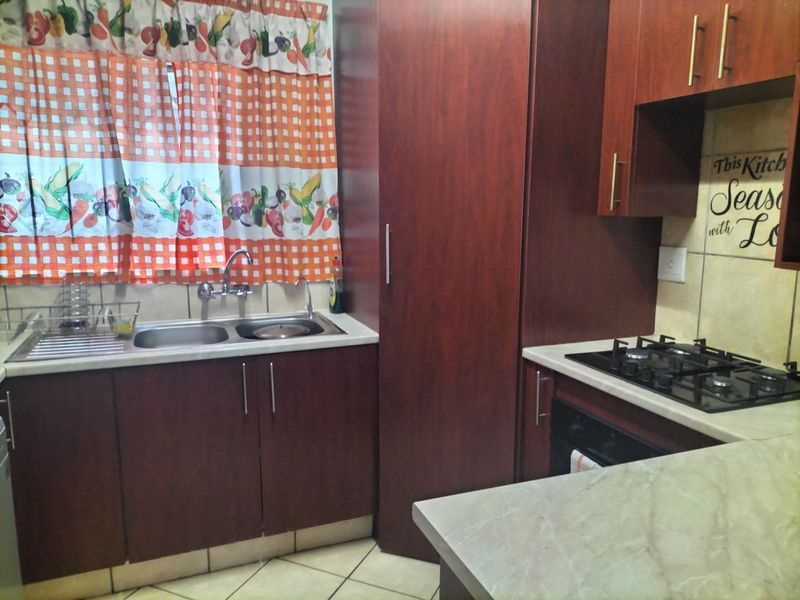 A functional kitchen featuring dark wood cabinetry, laminate countertops, a gas hob, built-in oven, and a double basin sink with tiled finishes.