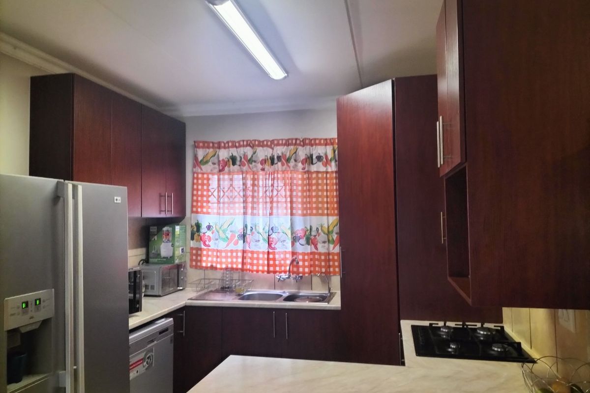 A functional kitchen featuring dark wood cabinetry, a gas hob, laminate countertops, and a double sink with a window view.