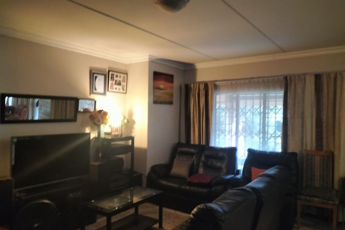 A comfortable living room featuring tiled flooring, ceiling cornicing, and a security gate over the window, providing a functional and lived-in space.