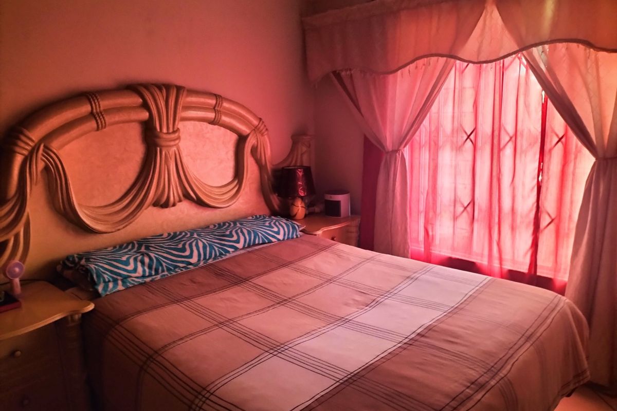 A bedroom featuring a window with security gate and draped curtains, providing a functional sleeping space.
