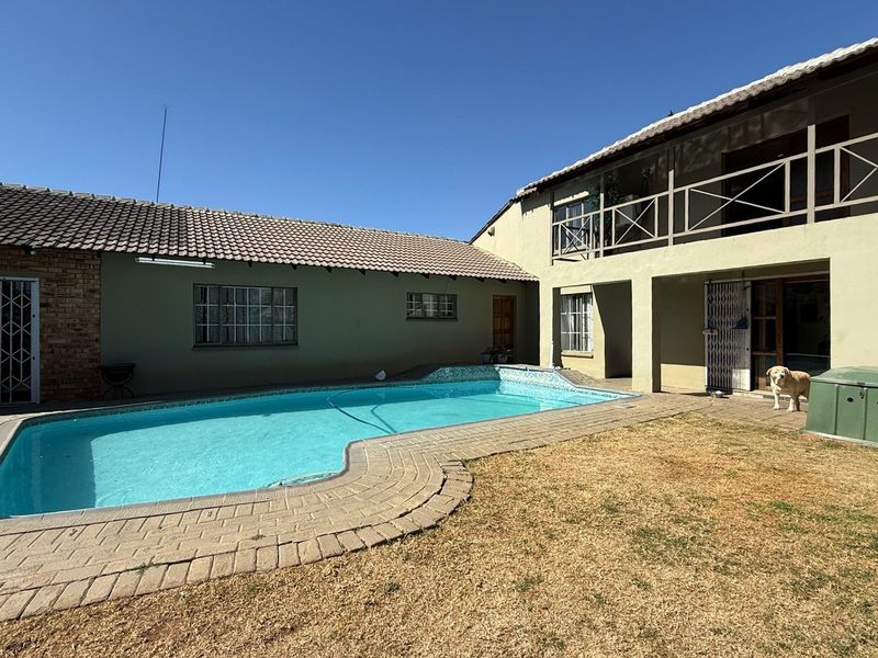 Rear exterior view featuring a swimming pool, brick paved surround, and a two-story building structure with a balcony.