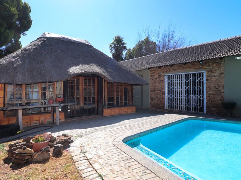 Outdoor pool area featuring a traditional thatch-roof lapa, brick paving, and a swimming pool set against an exposed brick exterior wall.