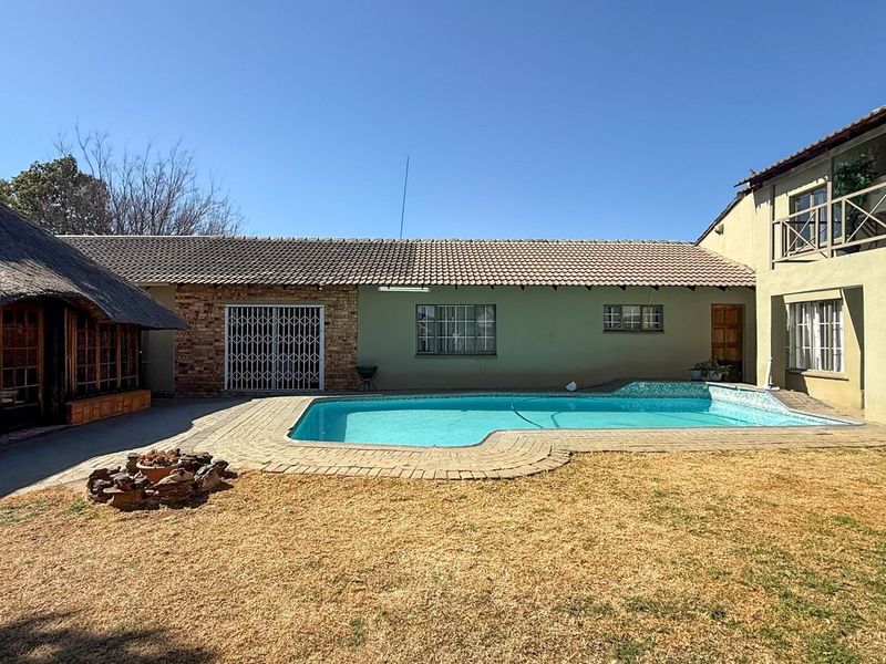 Outdoor pool area featuring a swimming pool, paved surround, and an adjacent thatched lapa structure with a two-story building facade.