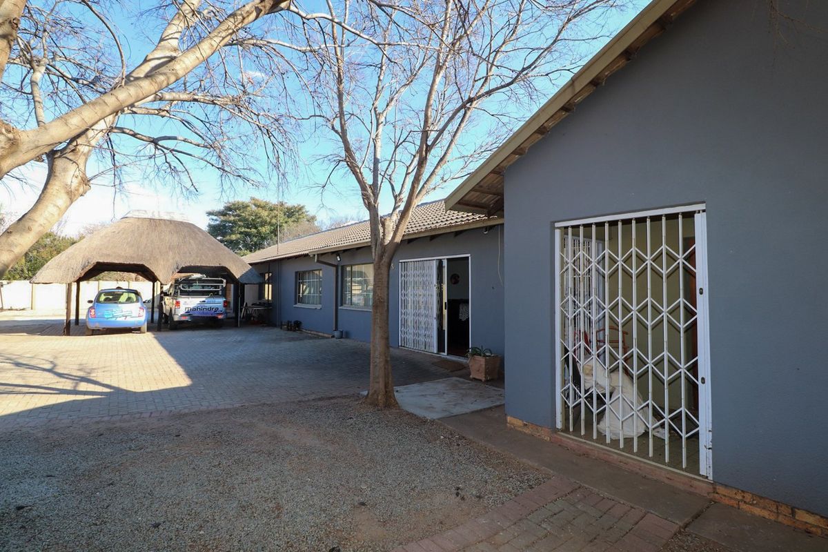 Rear exterior view of the property featuring a paved driveway, a thatched roof carport, and secure access points with fitted security gates.