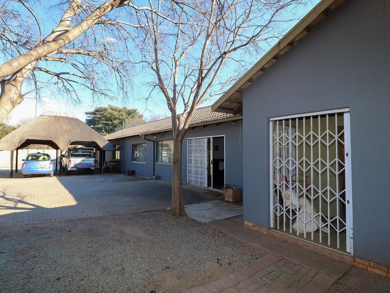Rear exterior view of the property featuring a paved driveway, a thatched roof carport, and secure access points with fitted security gates.