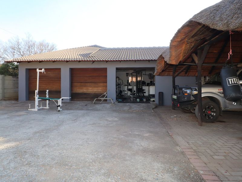 A triple garage with timber doors and an adjacent thatched roof carport, featuring a concrete driveway and paved parking area.