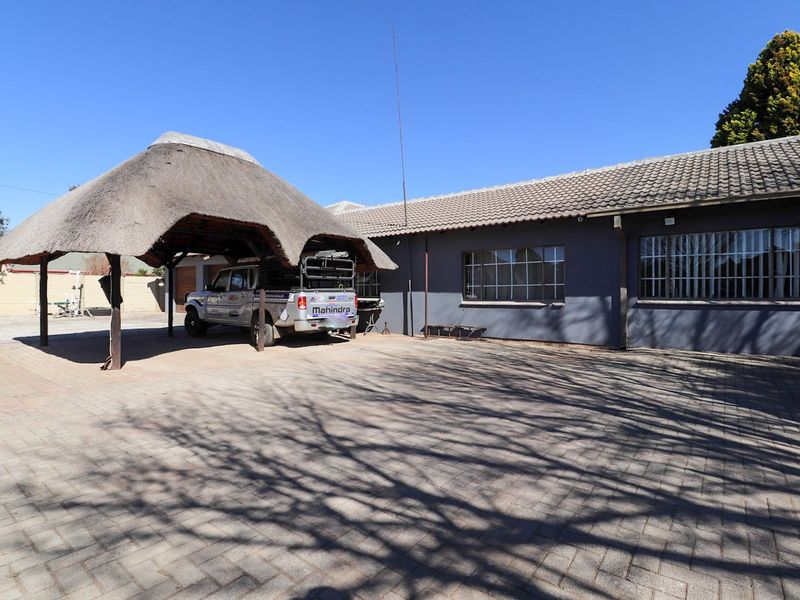 Front exterior view of the property featuring a paved driveway, a thatched roof carport, and a single-story building with security-barred windows.