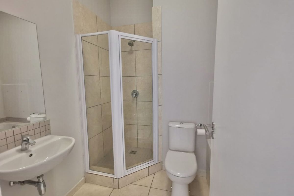A clean and functional bathroom featuring a corner shower enclosure, wall-mounted basin, and toilet with neutral tiled finishes.