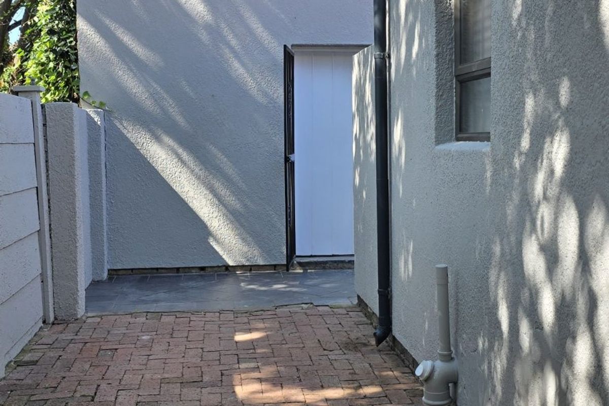 A side exterior view showing a brick-paved pathway leading to a rear entrance, featuring textured exterior walls and a drainage downpipe.