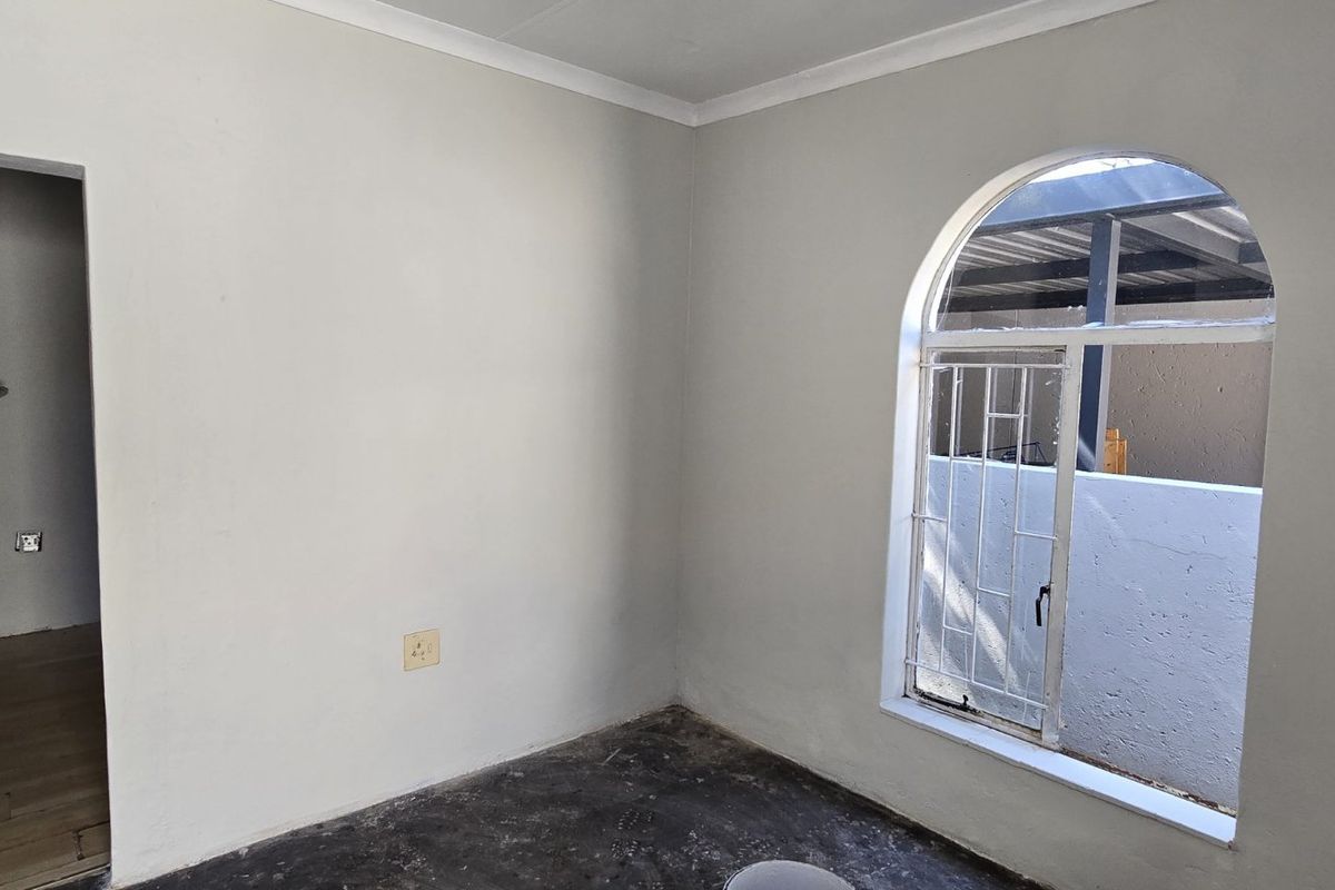 An empty bedroom featuring a distinctive arched window with security bars and an adjacent doorway leading to a secondary space.