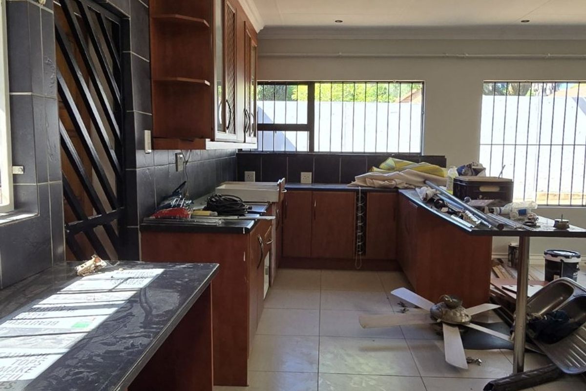 A spacious kitchen area featuring dark tiled splashbacks, wooden cabinetry, and large floor tiles, currently undergoing renovation or maintenance.