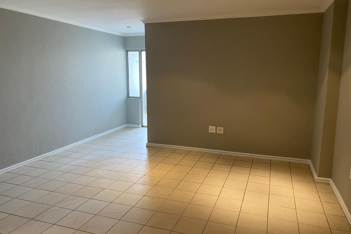 A spacious, empty living area featuring neutral-toned walls, ceramic tiled flooring, and recessed downlighting, offering a clean and versatile blank canvas.