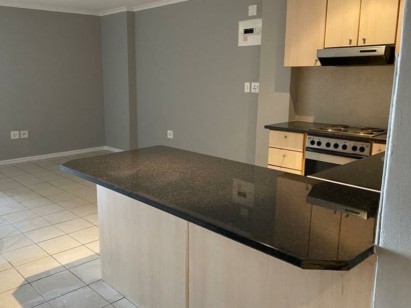 Open plan living area featuring a kitchen with granite countertops, built-in cabinetry, and an integrated electric stove, finished with neutral tiled flooring.