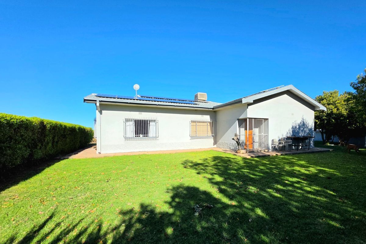 Rear view of the house featuring a well-maintained lawn, paved patio area, and roof-mounted solar panels.