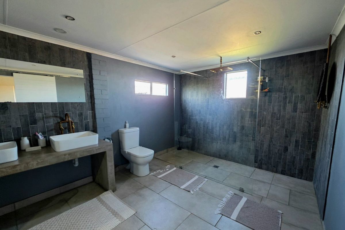 Modern bathroom featuring a double vanity with concrete countertop, walk-in shower with glass screen, rain shower head, and contemporary dark tiled wall finishes.