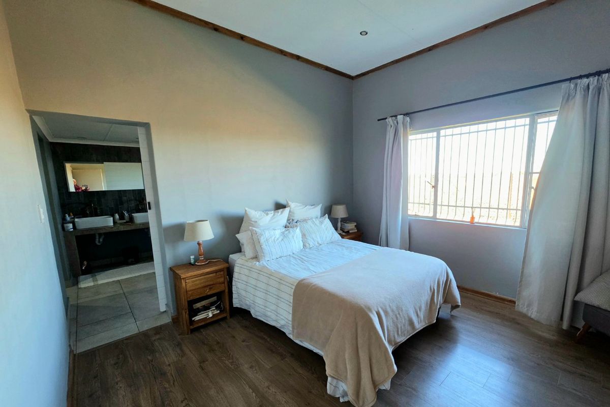 A well-maintained bedroom featuring laminate flooring, natural light through security-fitted windows, and direct access to an en-suite bathroom.