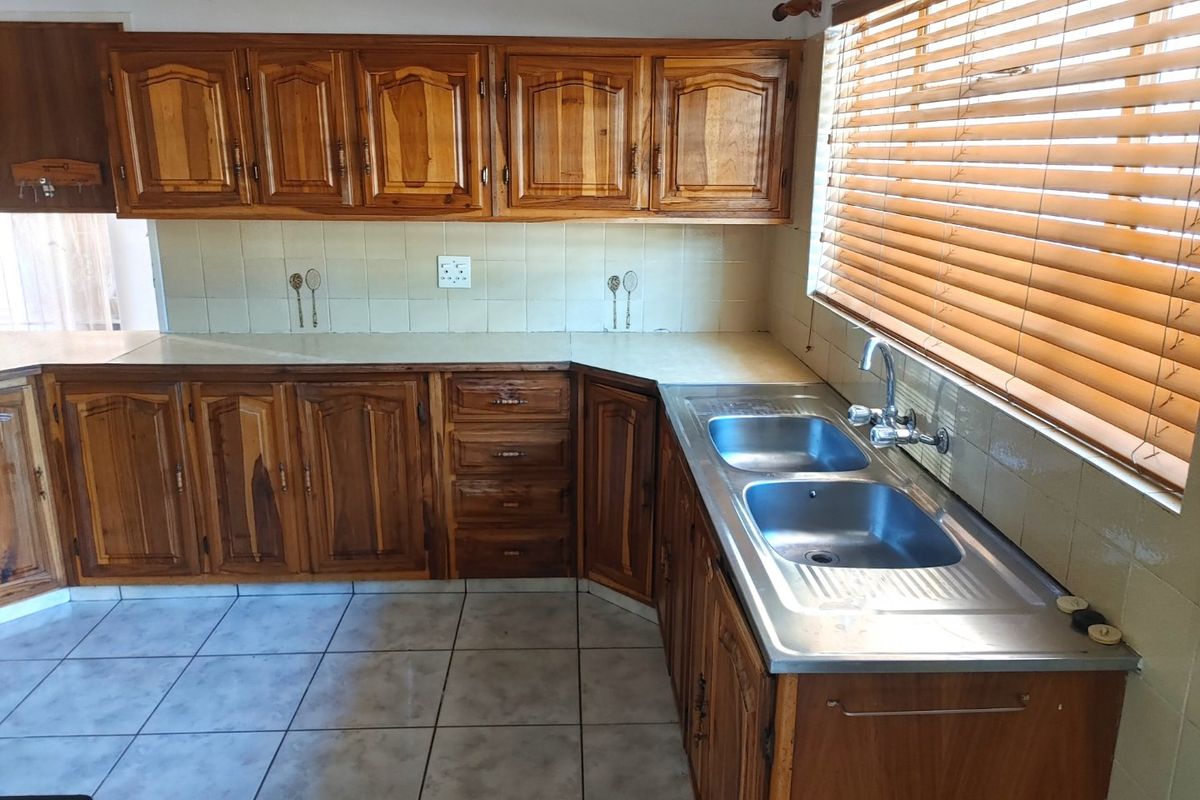 A functional kitchen featuring traditional timber cabinetry, a double stainless steel sink, and tiled flooring with ample counter space.