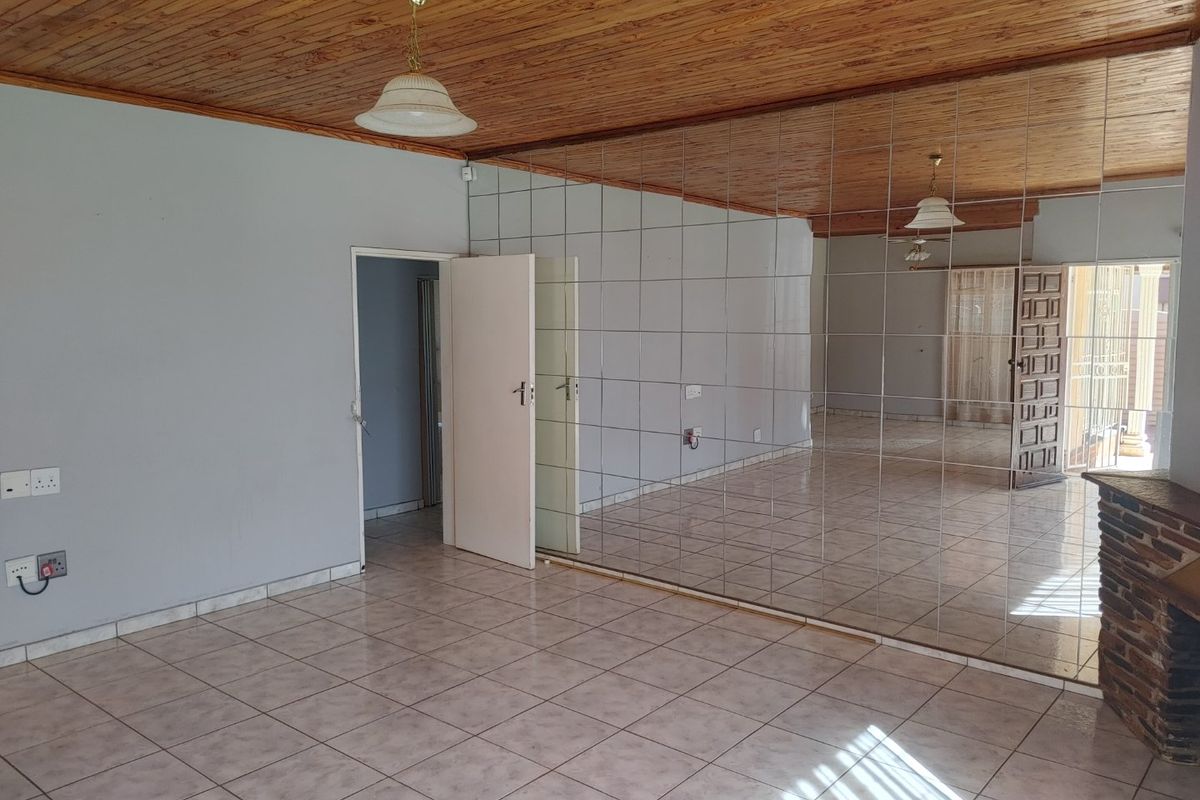 Spacious living area featuring tiled flooring, a distinctive wooden ceiling, and a large mirrored wall, offering a blank canvas for renovation.
