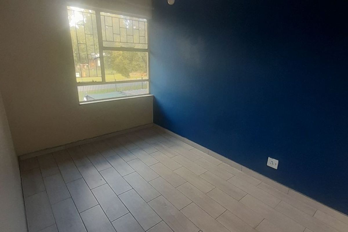 An empty bedroom featuring light-colored tiled flooring, a large window with security bars, and a bold blue accent wall.