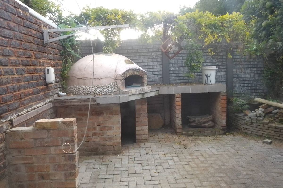 Outdoor entertainment area featuring a built-in brick pizza oven and braai station set within a paved garden space.