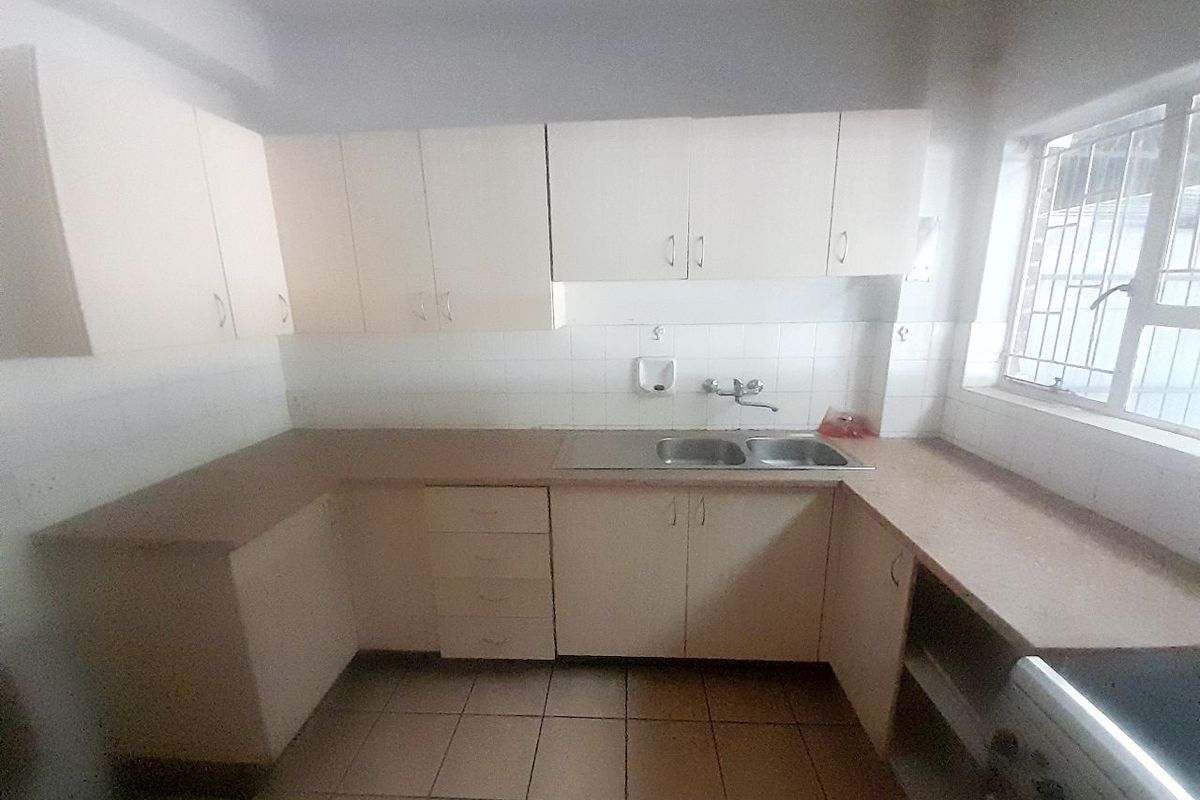 A dated, empty kitchen featuring laminate countertops, built-in cabinetry, a double basin sink, and tiled flooring, offering potential for a modern renovation.