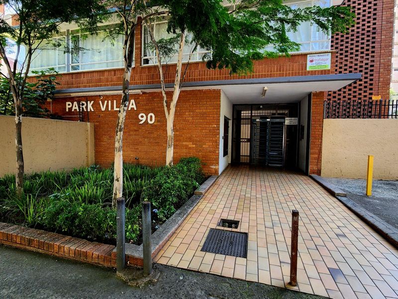 Front entrance view of Park Villa apartment complex featuring a brick facade, paved walkway, and secure gated access.