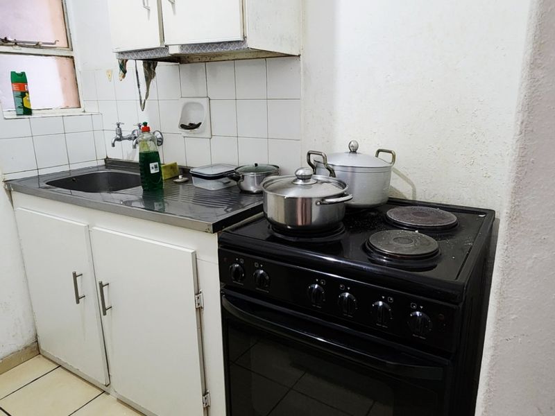 Compact kitchen featuring white cabinetry, a stainless steel sink, tiled backsplash, and a freestanding electric stove with oven.