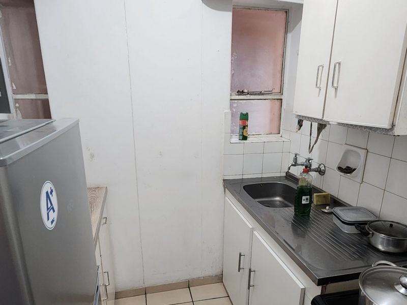A compact kitchen featuring a stainless steel sink, tiled backsplash, and built-in cabinetry, offering a functional layout in need of cosmetic updates.