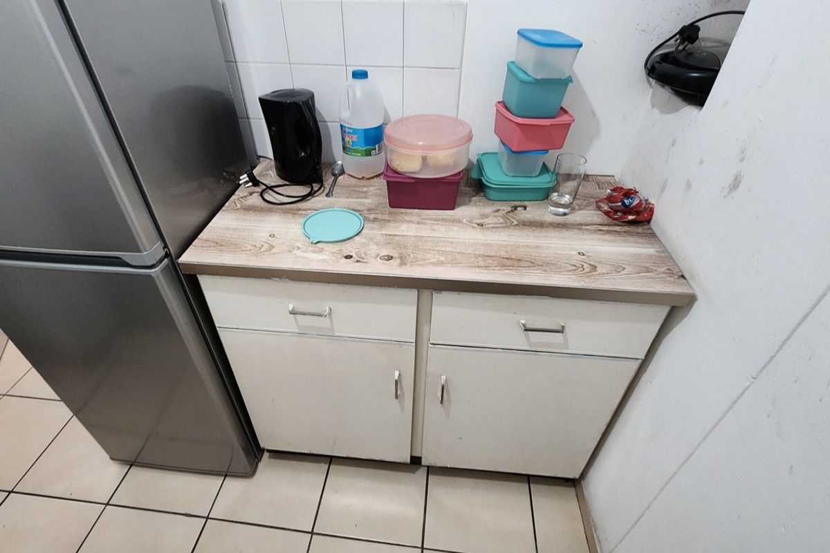 A compact kitchen area featuring laminate countertops, base cabinetry, and tiled splashbacks, showing signs of wear and wall staining.